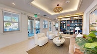 Located at 13901 SW 122nd Ave in Miami, FL, this expansive single-floor amenity center offers a well-rounded collection of community spaces designed for both relaxation and activity. The welcoming entryway features light hardwood-style flooring, curated artwork, lush greenery, and a sculptural pendant light that sets an inviting tone throughout.

The main lounge and living area showcases soaring vaulted ceilings with exposed white-painted beams, a dramatic teal accent wall, and a built-in media console with a fireplace surround. A large ceiling fan, comfortable seating, and original artwork create a warm, resort-inspired atmosphere. Adjacent to this, the kitchen and billiards area continues the vaulted ceiling aesthetic, featuring a white quartz island, woven rattan pendant lights, bar seating, and a full-size pool table — ideal for social gatherings.

A separate lounge area offers a coffered tray ceiling with ambient lighting, built-in shelving, and curated décor, providing a quieter retreat. The two fitness rooms are extensively equipped with treadmills, cycling bikes, cable machines, free weights, and more, all bathed in natural light from large clerestory windows and cooled by oversized ceiling fans. Additional spaces include a private office nook with bold accent wallcovering and a bright conference room with natural light and ample seating.