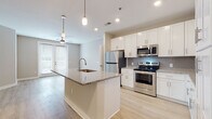 Located at 1321 Farrells West Ave in Henrico, Virginia, this single-floor residence offers a clean, contemporary design throughout. The open-concept kitchen serves as the heart of the home, featuring white shaker cabinetry, granite countertops, a tile backsplash, and a full suite of stainless steel appliances including a refrigerator, electric range, and over-the-range microwave. A large kitchen island with an undermount sink and pendant lighting above provides ample workspace and casual seating. Light-toned hardwood-style flooring flows seamlessly throughout the main living areas, complementing the neutral wall tones and crisp white trim. The living area benefits from natural light streaming through multiple windows dressed with horizontal blinds, and ceiling fans are present in several rooms for added comfort. The bedrooms are generously sized, each offering multiple windows, ceiling fans, and access to closet space—including at least one walk-in closet with built-in shelving. The bathrooms are finished with marble-look tile flooring, granite-topped white vanities, and chrome fixtures. One bathroom features a tub-shower combo with white subway tile surround, while another offers a glass-enclosed walk-in shower, providing versatile options for residents.
