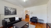 This single-floor residence combines classic architectural charm with functional, modern living. The inviting living room features warm hardwood flooring, crisp white walls, and a distinctive arched doorway that connects seamlessly to the adjoining area. The space is furnished with tufted black leather seating, a central coffee table, and a patterned area rug, creating a cohesive and comfortable atmosphere. Natural light filters through slatted blinds, enhancing the room's airy feel.

Through the arch, a compact dining and kitchenette area provides practical utility, with a stainless steel gas range, granite countertops, white cabinetry, and a stainless steel sink — a well-equipped kitchen that balances style and function.

The bedroom is bright and generously proportioned, showcasing rich hardwood floors, large windows that admit ample natural light, a ceiling fan with a light fixture, and a classic cast-iron radiator. An additional room with a closet and a wall-mounted HVAC unit offers flexible use as a second bedroom or office space.

The bathroom maintains a timeless aesthetic with white subway-style wall tiles, black-and-white mosaic floor tiles, a pedestal sink with brushed nickel fixtures, a mirrored medicine cabinet, and a shower-tub combination — clean, classic, and well-maintained throughout.