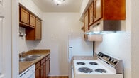 This single-floor residence offers a straightforward and functional layout designed for comfortable everyday living. The galley-style kitchen is efficiently organized with warm wood-toned cabinetry, granite-look countertops, a stainless steel sink, and white appliances including a coil-burner electric range, refrigerator, and dishwasher. An overhead range hood and ample upper and lower cabinet storage complete the space, which also features easy-to-clean wood-look flooring.

The living area is bright and open, with large windows dressed in vertical blinds that allow natural light to fill the room. A combination of wood-look flooring near the entryway and neutral carpet throughout the living and bedroom spaces adds warmth and texture. The textured walls and standard ceiling height give the space a classic residential feel.

The bedroom is a quiet, carpeted room with its own window fitted with vertical blinds, providing natural light and privacy. A hallway connects the main living areas and offers access to additional storage.

The bathroom is clean and well-appointed, featuring a full soaking tub and shower combination with a white surround, wood-look flooring, granite-look countertop, and brushed nickel hardware. The overall ambiance of the unit is neutral, tidy, and move-in ready.