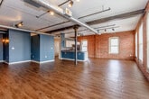 Located at 207 Walnut St in the heart of Kansas City, MO, this single-floor urban loft masterfully blends industrial heritage with contemporary design. The expansive open-concept living area is defined by rich hardwood-style flooring, bold teal accent walls, and original exposed brick that stretches across multiple walls, lending an authentic historic character. Overhead, raw steel beams, exposed ductwork, and track lighting reinforce the industrial aesthetic while providing both functionality and visual interest. Structural steel columns punctuate the main living space, adding to its loft-style appeal.

The kitchen is well-appointed with white cabinetry, a mosaic tile backsplash, dark countertops, stainless steel appliances including a double oven and full-size refrigerator, and a peninsula that opens to the main living area. Arched windows along the brick exterior wall flood the space with natural light and offer views of the surrounding downtown streetscape.

The bedroom features carpeted flooring, exposed brick walls, and large windows with city views, creating a comfortable urban retreat. A spacious walk-in closet with built-in shelving and hanging rods provides generous storage. The bathroom is finished with cork-style flooring, a wood-toned vanity with a dark countertop, and a full tub-shower combination, offering a clean and functional design.