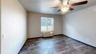 Located at 3411 Jaffa Garden Way in Rapid City, South Dakota, this single-floor 1-bedroom unit offers a practical and comfortable layout designed for efficient living. The combined kitchen and living area forms the heart of the unit, featuring durable wood-look plank flooring, neutral-toned walls, and flush ceiling lighting that keeps the space feeling bright and open. The kitchen stands out with its crisp grey shaker-style cabinetry, light stone countertops, a double-basin sink, and a full suite of stainless steel appliances including a refrigerator, dishwasher, electric range, and microwave — all accented by a pendant light above the sink area. The open living space connects seamlessly to the kitchen, providing a flexible area for everyday use, and includes a ceiling fan with a light fixture for added comfort. The bedroom offers a cozy retreat, finished with plush carpeting, a window that allows natural light to filter in, and convenient access to a dedicated closet. Dark baseboards provide a clean contrast throughout, adding a subtle design element that ties the space together. The overall ambiance is clean, modern, and move-in ready, making this unit a functional and comfortable home in Rapid City.