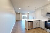 Located at 1920 Gregg Rd in Bellevue, Nebraska, this well-appointed one-bedroom, one-bathroom residence offers a thoughtfully designed open-concept floor plan. The combined living, dining, and kitchen area serves as the heart of the home, featuring warm wood-look plank flooring, recessed lighting, and a sliding glass door that opens to a private balcony with outdoor views. The modern kitchen is outfitted with gray shaker-style cabinetry, crisp white countertops, a peninsula with an undermount sink, and a full suite of stainless steel appliances including a refrigerator, range, microwave, and dishwasher. Stylish pendant lights above the peninsula add an elegant finishing touch. The spacious bedroom is carpeted for comfort and includes a ceiling fan, a large window for natural light, and access to a generously sized walk-in closet with dual hanging rods and built-in shelving. The bathroom features a wide vanity with white countertops, gray cabinetry with brushed nickel hardware, and a large mirror. Additional conveniences include a dedicated laundry area and multiple closets throughout, providing ample storage. The neutral color palette and clean modern finishes create a bright, welcoming ambiance throughout.