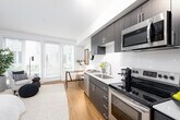 Located at 15560 Westminster Way N in Shoreline, Washington, this single-floor residence offers a thoughtfully designed layout with modern finishes and a clean, contemporary aesthetic. A welcoming entryway hallway with warm hardwood-style flooring leads into the main living areas, setting a cohesive tone throughout the unit. The kitchen is a standout feature, outfitted with dark espresso cabinetry, white quartz countertops, a classic subway tile backsplash, and a full suite of stainless steel appliances including a dishwasher, range, microwave, and refrigerator. Track lighting overhead adds a modern touch. The living area is bright and airy, benefiting from large windows with horizontal blinds that allow natural light to filter in while offering a view of the surrounding neighborhood. The bedroom is a serene retreat with a ceiling fan, soft neutral tones, and hardwood-style flooring, providing a calm and comfortable atmosphere. The bathroom features dark wood cabinetry with a white countertop vanity, a large mirror, and hardwood-style flooring, maintaining the consistent modern design language found throughout the space. Overall, this residence combines functional design with stylish details to create a comfortable and well-appointed living environment.