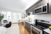 Located at 15560 Westminster Way N in Shoreline, Washington, this single-floor residence offers a thoughtfully designed layout with modern finishes and a clean, contemporary aesthetic. A welcoming entryway hallway with warm hardwood-style flooring leads into the main living areas, setting a cohesive tone throughout the unit. The kitchen is a standout feature, outfitted with dark espresso cabinetry, white quartz countertops, a classic subway tile backsplash, and a full suite of stainless steel appliances including a dishwasher, range, microwave, and refrigerator. Track lighting overhead adds a modern touch. The living area is bright and airy, benefiting from large windows with horizontal blinds that allow natural light to filter in while offering a view of the surrounding neighborhood. The bedroom is a serene retreat with a ceiling fan, soft neutral tones, and hardwood-style flooring, providing a calm and comfortable atmosphere. The bathroom features dark wood cabinetry with a white countertop vanity, a large mirror, and hardwood-style flooring, maintaining the consistent modern design language found throughout the space. Overall, this residence combines functional design with stylish details to create a comfortable and well-appointed living environment.