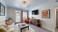 This thoughtfully designed single-floor residence offers a cohesive and welcoming living environment finished with wood-look flooring, crown molding, and a neutral color palette throughout. The living room serves as the heart of the home, bathed in natural light streaming through large windows framed by bold red-patterned curtains. A decorative pendant ceiling fixture adds charm, while a private exterior door provides convenient outdoor access. The kitchen is well-equipped with rich dark cabinetry, granite-style countertops, stainless steel appliances including a refrigerator, range, and built-in microwave, and a classic subway tile backsplash that ties the space together. Adjacent to the kitchen, the dining area features an elegant pendant light and offers a cozy setting for everyday meals. Both bedrooms are generously proportioned, each featuring crown molding, ceiling fans, large windows, and walk-in closets with built-in storage. The full bathroom includes a dark-toned vanity with ample counter space, a combined tub and shower with a curtain enclosure, and wood-look flooring that complements the rest of the home. Every room reflects a consistent design language that balances comfort with practicality.