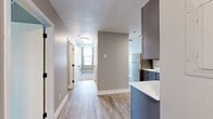 This single-floor residence offers a thoughtfully designed layout with a clean, contemporary aesthetic. The kitchen serves as a functional centerpiece, featuring grey cabinetry with ample upper and lower storage, light-toned countertops, a undermount sink with a matte black faucet, and a full suite of stainless steel appliances including a refrigerator, dishwasher, electric range, and over-the-range microwave. Light wood-look flooring runs through the kitchen and hallway, lending warmth and easy maintenance to the main living areas.

A central hallway connects the various rooms, providing a clear and organized flow throughout the unit. The bedrooms are finished with neutral carpet and warm taupe-toned walls, creating a calm and comfortable atmosphere. Notably, the bedrooms benefit from elevated city views through large windows, offering broad urban panoramas that bring in natural light. One bedroom includes a sliding double-door closet, maximizing storage efficiency.

The bathroom features wood-look tile flooring, a full soaking tub with a curved shower rod, matte black hardware accents, and clean white fixtures. Throughout the unit, white baseboards and neutral wall tones create a cohesive, modern feel that complements the overall design.