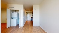 Located at 278 N Hancock St in Portland, Oregon, this efficient one-bedroom, one-bathroom unit offers a well-designed layout across a single floor. Light wood-tone flooring runs throughout, creating a cohesive and bright aesthetic.

The galley-style kitchen is a standout feature, showcasing sleek dark cabinetry that extends floor to ceiling, dark granite countertops, and a full suite of Whirlpool stainless steel appliances including an electric range, over-the-range microwave, dishwasher, and refrigerator. Under-cabinet lighting adds a polished finish to the space.

The open living area is bright and clean, with crisp white walls that maximize the sense of openness. A large picture window in the bedroom frames a remarkable panoramic view of the Portland skyline and a prominent bridge — a compelling architectural highlight. The bedroom offers a comfortable footprint with a dedicated closet for storage.

The bathroom features tile flooring in a wood-look finish, a soaking tub, and clean white fixtures with matte black hardware accents. A notable convenience is the in-unit stacked washer and dryer, housed in a dedicated closet off the main living area. The overall design balances modern, urban aesthetics with practical functionality.