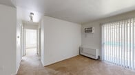 This single-story, 2-bedroom, 1-bathroom unit offers a straightforward and functional layout designed to maximize its compact footprint. The living area features neutral-toned carpet, crisp white walls, and a wall-mounted air conditioning unit alongside a baseboard heater, ensuring year-round climate control. A sliding glass door with vertical blinds provides natural light and exterior access.

The kitchen is laid out in a galley configuration, equipped with warm-toned wooden cabinetry offering ample upper and lower storage, light-colored countertops, a stainless steel sink, and white appliances including a range and refrigerator. The flooring is a durable tile-style surface suited for the space.

Both bedrooms are carpeted and finished with white walls. The primary bedroom is a comfortable size and features an expansive wall of louvered bi-fold closet doors, providing notable storage capacity. The second bedroom includes a window with blinds, allowing natural light to enter. Both rooms include overhead ventilation.

The bathroom is distinguished by its retro light-blue ceramic tile surround enclosing a full bathtub, complemented by a window with blinds that introduces natural light. The overall aesthetic throughout the unit is clean and neutral.
