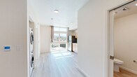 Located at 2701 Shattuck Ave in Berkeley, CA, this thoughtfully designed single-floor unit offers a clean, modern aesthetic throughout. Light-toned wood-style flooring runs seamlessly across all areas, complementing the crisp white walls and recessed lighting that give the space an airy, well-lit feel.

The open main area connects the living space to a functional kitchenette, which features warm-toned light wood cabinetry, a stainless steel refrigerator, a built-in sink with clean countertops, and large floor-to-ceiling windows that flood the space with natural light and frame sweeping views of the Berkeley Hills and surrounding neighborhood rooftops.

A dedicated alcove houses a full-size stacked washer and dryer unit, providing convenient in-unit laundry. A wall-mounted mini-split system ensures year-round climate comfort. The bathroom is finished in a neutral palette with light wood-look tile flooring, a pedestal sink, and a full toilet — clean and functional in its design.

The bedroom area benefits from oversized windows that deliver an abundance of natural light and picturesque hillside views, creating a serene and uplifting atmosphere. The overall design of this unit prioritizes brightness, efficiency, and a connection to the natural surroundings of the Berkeley landscape.