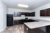 Located at 2835 S Goship Ln in Magna, Utah, this single-floor residence offers three bedrooms, two bathrooms, and a thoughtfully laid-out floor plan. The combined kitchen and living area serves as the heart of the home, featuring rich dark espresso cabinetry with ample upper and lower storage, granite-style countertops, black appliances including a refrigerator and range, and a breakfast bar peninsula ideal for casual dining. Wood-style plank flooring runs throughout the main living areas, adding warmth and durability. The living room is bright and open, highlighted by a ceiling fan and sliding glass doors fitted with vertical blinds that lead to a private balcony with outdoor views. The three bedrooms are carpeted for comfort, with the generously sized primary bedroom offering a walk-in closet equipped with wire shelving and hanging rods. Two full bathrooms serve the home — one featuring a tub-shower combo with accessible grab bars and wood-style flooring, and the other offering a tub-shower enclosure, a dark-cabinetry vanity with a granite-style countertop, and matching flooring. A hallway connects the bedrooms efficiently, and two closets provide additional storage throughout the home.