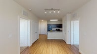 This single-floor residence offers a thoughtfully designed open-concept layout that seamlessly connects the living area to the kitchen. Warm wood-style flooring extends throughout the main living spaces, creating a cohesive and inviting atmosphere. The kitchen is a functional centerpiece, featuring dark cabinetry, granite-style countertops, a peninsula with a built-in sink, and a full suite of black appliances including a refrigerator, range, and microwave. Track lighting overhead provides ample illumination. The open hallway leads to multiple well-proportioned bedrooms, each finished with plush carpeting, ceiling fans with light fixtures, and windows fitted with blinds that allow for natural light. The primary bathroom includes a tub-shower combination, a dark-cabinetted vanity with a single sink, and direct access to a walk-in closet with built-in shelving. A second full bathroom mirrors the same clean, neutral aesthetic. Throughout the unit, neutral wall tones, white trim, and consistent flooring choices contribute to a bright, clean, and functional living environment suited for comfortable everyday living.