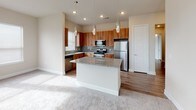 This single-floor residence offers a thoughtfully designed layout with a cohesive blend of warm wood tones, neutral walls, and quality finishes throughout. The kitchen serves as a central highlight, featuring rich medium-toned wood cabinetry, a tile backsplash, stainless steel appliances including a range, microwave, dishwasher, and refrigerator, and a granite-topped island with pendant lighting overhead. Wood-look flooring runs through the kitchen and connects seamlessly to adjacent areas. The living area is carpeted and generously sized, with a ceiling fan and access to a door that leads outside, allowing natural light to fill the room. Additional carpeted rooms offer ceiling fans and windows with blinds, providing comfortable, flexible spaces. The primary bathroom features wood-look flooring, a granite vanity with warm wood cabinetry, a walk-in glass shower, and direct access to a walk-in closet with built-in shelving. A secondary bathroom includes a granite vanity, matching wood cabinetry, wood-look flooring, and a soaking tub with a curved shower rod and grab bars for added convenience. The overall ambiance is clean, modern, and functional.