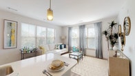 This single-floor residence at Alta offers a thoughtfully designed, open-concept layout filled with natural light throughout. The living area serves as the heart of the home, featuring wide-plank wood-style flooring, multiple large windows dressed with elegant drapes and wood blinds, and a pendant light fixture that anchors the space. The seamless flow between the living and dining areas creates a welcoming, airy atmosphere ideal for both relaxing and entertaining.

The kitchen is well-appointed with white shaker-style cabinetry extending to the ceiling for ample storage, a classic subway tile backsplash, light quartz countertops, and a full suite of stainless steel appliances including a range, microwave, and refrigerator. Wood-style flooring continues throughout this space, adding warmth and cohesion.

The bedroom is a serene retreat, featuring plush carpeting, dual windows with natural views, and direct access to a generous walk-in closet. A versatile secondary room with carpeting and a window provides an ideal flex space suitable as a den or home office.

Two bathrooms serve the residence: one features a single vanity with quartz counters, a tiled tub-shower combination, and wood-style flooring, while the second offers a clean, streamlined design with a single vanity and a separate shower area.