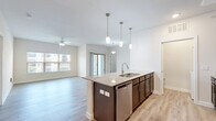 This single-story, 3-bedroom, 2-bathroom residence offers a clean, modern design with an efficient and functional layout. The open-concept kitchen and living area serves as the heart of the home, anchored by a central island with granite countertops, an undermount sink, and elegant pendant lighting. Dark espresso cabinetry contrasts beautifully with the white subway tile backsplash, while stainless steel appliances — including a refrigerator, range, and microwave — complete the kitchen. Light wood-look flooring runs throughout the main living areas, complementing the bright, neutral color palette. The living room is well-lit by natural light from large windows and a sliding glass door, and is equipped with a ceiling fan for added comfort. Each bedroom features plush carpeting, natural light from windows, and dedicated closet space, with the primary bedroom offering a generously sized layout. Three closets throughout the unit provide ample storage. Both bathrooms are finished with granite-topped vanities, dark cabinetry, and fully tiled shower-tub combinations with wood-look flooring. A laundry area is also conveniently located within the unit. Overall, the space presents a cohesive, contemporary aesthetic with quality finishes throughout.