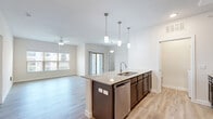 This single-story, 3-bedroom, 2-bathroom residence offers a clean, modern design with an efficient and functional layout. The open-concept kitchen and living area serves as the heart of the home, anchored by a central island with granite countertops, an undermount sink, and elegant pendant lighting. Dark espresso cabinetry contrasts beautifully with the white subway tile backsplash, while stainless steel appliances — including a refrigerator, range, and microwave — complete the kitchen. Light wood-look flooring runs throughout the main living areas, complementing the bright, neutral color palette. The living room is well-lit by natural light from large windows and a sliding glass door, and is equipped with a ceiling fan for added comfort. Each bedroom features plush carpeting, natural light from windows, and dedicated closet space, with the primary bedroom offering a generously sized layout. Three closets throughout the unit provide ample storage. Both bathrooms are finished with granite-topped vanities, dark cabinetry, and fully tiled shower-tub combinations with wood-look flooring. A laundry area is also conveniently located within the unit. Overall, the space presents a cohesive, contemporary aesthetic with quality finishes throughout.