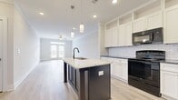 Located at 5025 Pilatus Way in Mebane, NC, this well-appointed 2-bedroom, 2-bathroom single-story home offers a thoughtfully designed open-concept layout. The kitchen is a standout centerpiece, featuring a large island with striking granite countertops, a contrast dark base, an undermount sink with a matte black faucet, crisp white shaker cabinetry extending to the ceiling, classic subway tile backsplash, and black appliances including a range, microwave, and refrigerator. Pendant lighting and recessed fixtures illuminate the space, which flows seamlessly into the bright living room. The living area is finished with light wood-look flooring and is anchored by French doors topped with a transom window, inviting abundant natural light and outdoor views. A ceiling fan adds comfort to both the living room and bedrooms. The spacious primary bedroom features plush carpeting, multiple windows framing outdoor views, and direct access to a walk-in closet outfitted with wire shelving. The bathrooms are clean and modern, with one featuring a soaking tub and matte black fixtures. A dedicated laundry room with wood-look flooring and built-in shelving adds everyday convenience, completing this functional and stylish home.