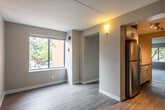 This single-floor unit offers a clean, modern interior with a cohesive neutral color palette and wood-style flooring that runs throughout the space. The open living area is bathed in natural light from a large window overlooking mature trees, creating a calm and inviting atmosphere. A textured ceiling and warm-toned walls add subtle character to the main living spaces.

The galley-style kitchen is a standout feature, thoughtfully designed with white shaker cabinetry, granite-look countertops on both sides, stainless steel appliances including a range, over-the-range microwave, and refrigerator, along with track lighting overhead. The layout maximizes counter and storage space efficiently.

The bedroom areas are generously sized, each with neutral walls and wood-style flooring. One bedroom features a large window with views of the surrounding greenery, while another includes a double-door closet for ample storage. The rooms provide a versatile, move-in-ready canvas.

The bathroom is neatly finished with a white vanity featuring a granite-top countertop, a full tub-shower combination with clean tile surround, and light wood-style flooring. Throughout the unit, white trim and baseboards provide a crisp contrast to the warm neutral walls, lending a polished, updated feel to the entire space.