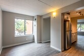 This single-floor unit offers a clean, modern interior with a cohesive neutral color palette and wood-style flooring that runs throughout the space. The open living area is bathed in natural light from a large window overlooking mature trees, creating a calm and inviting atmosphere. A textured ceiling and warm-toned walls add subtle character to the main living spaces.

The galley-style kitchen is a standout feature, thoughtfully designed with white shaker cabinetry, granite-look countertops on both sides, stainless steel appliances including a range, over-the-range microwave, and refrigerator, along with track lighting overhead. The layout maximizes counter and storage space efficiently.

The bedroom areas are generously sized, each with neutral walls and wood-style flooring. One bedroom features a large window with views of the surrounding greenery, while another includes a double-door closet for ample storage. The rooms provide a versatile, move-in-ready canvas.

The bathroom is neatly finished with a white vanity featuring a granite-top countertop, a full tub-shower combination with clean tile surround, and light wood-style flooring. Throughout the unit, white trim and baseboards provide a crisp contrast to the warm neutral walls, lending a polished, updated feel to the entire space.