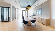 Located at 700 Northeast 1st Avenue in the heart of Miami, FL, this single-floor office suite offers a thoughtfully designed workspace that balances functionality with sophisticated aesthetics. The layout includes a conference room, an open collaborative area, a private office, and a connecting hallway.

The conference room serves as a centerpiece, featuring a large dark wood table surrounded by ergonomic chairs, bold matte-black pendant lights with gold interiors suspended from a teal-accented tray ceiling, and floor-to-ceiling windows that flood the space with natural light and offer sweeping views of the Miami skyline. Built-in cabinetry and a mounted display screen add practical utility.

The open collaborative area is anchored by a long communal table with plush velvet task chairs, complemented by striking black-and-gold dome pendant lighting. A lounge nook nearby features curved terracotta-red armchairs, minimalist side tables, and globe wall sconces, creating an inviting informal meeting space. Vertical wood slat wall panels in a neutral tone appear throughout, adding texture and visual continuity.

The private office is distinguished by a patterned area rug, a sleek desk, and dramatic floor-to-ceiling windows offering panoramic city views. Light oak hardwood flooring runs throughout, tying the spaces together with a warm, refined finish.