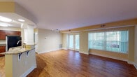 This single-floor residence is designed with a thoughtful layout that balances open communal spaces with comfortable private quarters. The living area is spacious and inviting, featuring warm hardwood flooring, soft cream-toned walls, and a track lighting fixture overhead. Natural light flows in through sliding glass doors and large vertical-blind-covered windows, which offer views to the outdoors. An open passage connects the living space to the kitchen, which is well-equipped with rich cherry wood cabinetry, granite countertops, stainless steel appliances including a range, microwave, and sink, alongside a black refrigerator. A decorative column accent adds architectural interest near the kitchen peninsula.

The bedrooms are carpeted and finished with the same warm wall tones, each featuring ceiling fans and windows that invite natural light. The primary bedroom includes a walk-in closet, additional storage, and direct access to an en-suite bathroom. The bathrooms are finished with granite vanity countertops, cherry wood cabinetry, and tiled tub-shower combinations with decorative mosaic accent borders. A second bathroom mirrors this clean, polished aesthetic. Consistent design details throughout create a cohesive and comfortable living environment.