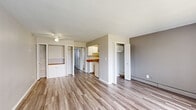 This compact yet efficiently designed one-bedroom, one-bathroom unit spans a single floor, making the most of every square foot. Throughout the space, wood-tone laminate flooring in a cool gray finish provides a cohesive and contemporary look.

The living room is a bright, open area anchored by a large window with vertical blinds that allow natural light to pour in while offering a view of the surrounding green outdoor space. A ceiling fan with a light fixture adds both comfort and function. Built-in shelving and cabinetry along one wall provide practical storage, while baseboard heating and a wall-mounted AC unit ensure year-round comfort.

The kitchen is a galley-style space featuring white cabinetry, warm wood-tone countertops, a stainless steel sink, and white appliances including a coil-top range and refrigerator — offering a clean, organized cooking environment.

The bedroom is a well-proportioned room with ample natural light from a large window with vertical blinds, a ceiling-mounted light fixture, and access to a dedicated closet. Baseboard heating runs along the perimeter walls.

The bathroom includes a wood-toned vanity with a white integrated countertop and sink, a large mirror, and overhead lighting. A hallway with a closet completes the efficient layout of this thoughtfully arranged unit.