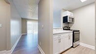 This single-story unit combines modern updates with a practical, well-organized layout. The galley-style kitchen is a standout feature, outfitted with crisp white shaker cabinetry, marble-look quartz countertops, a subway tile backsplash, and a full suite of stainless steel appliances including a gas range, microwave, refrigerator, and dishwasher. Light wood-style flooring runs through the kitchen and connects to an open pass-through that overlooks the living area, creating an airy, connected feel. The living room is generously proportioned, featuring a sliding glass door dressed with vertical blinds that brings in natural light and provides outdoor access. A wall-mounted air conditioning unit and baseboard heating ensure year-round comfort. The bedrooms are carpeted for warmth and comfort, each featuring textured ceilings, neutral walls, and ample natural light through standard windows with blinds. One bedroom includes a walk-in closet, offering practical storage. The bathroom features a full soaking tub and shower combination surrounded by clean white subway tile and brushed nickel fixtures. Throughout the unit, a neutral color palette and textured ceilings contribute to a cohesive, move-in-ready aesthetic.
