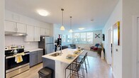 Located at 10 Patriot Parkway in South Weymouth, MA, this well-designed one-bedroom, one-bathroom residence offers a thoughtfully laid-out single floor of comfortable living space. The open-concept kitchen is a standout feature, showcasing two-tone cabinetry with crisp white upper cabinets and bold blue-gray lower cabinets, stainless steel appliances, a subway tile backsplash, and a large center island with a white quartz countertop and built-in sink — ideal for both meal preparation and casual dining. Light wood-style flooring flows throughout the main living areas, enhancing the bright, airy ambiance. The living room is generously proportioned, featuring large windows that invite abundant natural light and views of the surrounding neighborhood. The bedroom offers a cozy, well-sized retreat with plush carpeting, a window with outdoor views, and a dedicated closet for storage. The full bathroom is finished with gray subway tile in the tub/shower surround, tile flooring, a gray vanity with white countertop, and clean, modern fixtures. Throughout the residence, neutral white walls and contemporary finishes create a clean, modern aesthetic that is both inviting and versatile.