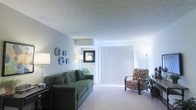 Located at 215 Prairie Creek Way in Columbus, Ohio, this single-floor residence offers a straightforward and functional layout designed for comfortable everyday living. The living room serves as the heart of the home, featuring neutral-toned carpeting and soft, light-colored walls that create a calm and inviting atmosphere. A large sliding glass door fitted with vertical blinds allows abundant natural light to fill the space while providing convenient access to the outdoors. The textured ceiling adds a classic architectural detail that complements the room's understated style. Decorative wall accents and thoughtfully placed lighting fixtures contribute to the room's warm ambiance. The space accommodates a generous seating arrangement, making it well-suited for relaxation and casual gatherings. The overall design emphasizes simplicity and livability, with a clean, open feel throughout. Situated in the east Columbus area, this home combines a practical single-level floor plan with a cozy interior aesthetic, making it an accessible and comfortable place to call home.