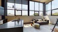Located at 230 East Ave in Norwalk, Connecticut, this modern loft-style residence showcases an industrial-inspired design with floor-to-ceiling grid windows that flood the open-concept living and kitchen area with abundant natural light and sweeping neighborhood views. Light-toned hardwood floors run throughout, creating a clean, cohesive aesthetic that complements the bold, dark-framed windows.

The kitchen is a standout feature, anchored by a substantial center island with a polished dark stone countertop and an integrated sink. Dark cabinetry lines the walls, paired with stainless steel appliances and a classic white tile backsplash. Pendant Edison bulb lighting adds an industrial warmth to the space. The living area flows seamlessly from the kitchen, benefiting from the same dramatic window wall and an airy, open atmosphere.

Two well-appointed bedrooms each feature large windows that invite natural light and offer views of the surrounding urban landscape, with light hardwood floors tying the rooms together. The bathrooms are thoughtfully designed — one features a glass-enclosed shower with vertical white tile and a dark-cabinetry vanity, while the second includes a full soaking tub with matching white tile surround. Together, these spaces offer a refined, contemporary urban living experience in the heart of Norwalk.