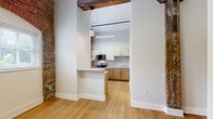 Located at 237-243 Furnace St in Akron, Ohio, this one-bedroom, one-bathroom unit offers a compelling blend of historic character and modern finishes. The space is defined by striking exposed red brick walls that carry throughout, serving as a testament to the building's industrial heritage. Soaring ceilings with visible ductwork and original timber beams add to the loft-like atmosphere, while arched windows allow natural light to pour in.

The kitchen is well-appointed with light wood cabinetry, white upper cabinets with black hardware, a double-basin stainless steel sink, a tile backsplash, stainless steel appliances including a range and over-the-range microwave, and light hardwood-style flooring. The exposed brick accent wall and arched window make this kitchen a standout feature of the unit.

The bedroom is generously proportioned, featuring wall-to-wall carpet, exposed brick on multiple walls, an arched window with natural light, and a double-door closet for ample storage. Soaring ceilings with an original wood beam add dramatic architectural interest.

The bathroom is clean and modern, featuring a tiled tub-shower combination with neutral subway-style tile, a wood-toned vanity with a white countertop, and hardwood-style flooring, creating a refreshing contrast to the unit's industrial elements.