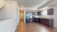 This two-floor residence is designed with a clean, functional aesthetic that carries consistently through each room. The open-concept main living area seamlessly connects to the kitchen, creating a spacious, unified environment ideal for both daily living and entertaining. Hardwood-style flooring in a warm, rich brown tone runs throughout the space, providing a cohesive visual foundation.

The kitchen is well-appointed, featuring dark espresso cabinetry with raised-panel detailing that extends from floor to ceiling, maximizing storage capacity. Granite-style countertops in a light speckled finish provide ample workspace and a polished contrast to the darker cabinetry. Black appliances — including a refrigerator, electric range, built-in microwave, and dishwasher — complete the kitchen suite. A window above the sink allows natural light to enter, brightening the workspace.

Recessed lighting throughout the main area, combined with a tray ceiling detail in the kitchen zone, adds architectural interest and depth. Additional rooms offer neutral, light-toned walls and the same continuous flooring, providing versatile, move-in-ready spaces. The bathroom features a granite-top vanity with an undermount sink, dark cabinetry below, and brushed nickel fixtures, maintaining the consistent, refined design language found throughout the home.