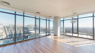 Located at 1908 Reston Station Blvd in Reston, Virginia, this high-rise residence is defined by its dramatic floor-to-ceiling glass walls that wrap around the main living areas, flooding the space with natural light and offering expansive panoramic views of the Reston skyline and surrounding landscape. The open living and dining area features warm hardwood flooring and an elegant globe chandelier, creating a sophisticated yet welcoming atmosphere.

The contemporary kitchen is outfitted with two-tone cabinetry in gray-wood and high-gloss white finishes, a neutral tile backsplash, light quartz countertops, a central island, and a full suite of stainless steel appliances including a gas range and built-in microwave.

The bedrooms are carpeted for comfort and benefit from large floor-to-ceiling windows that continue the unit's connection to the outdoors, with built-in closet systems providing ample storage. One bathroom features a freestanding soaking tub positioned directly beside the expansive glass wall, maximizing the elevated views, while a second bathroom offers a tiled tub-shower combination with clean, modern finishes throughout.