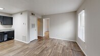 Located at 2050 Old Clinton Rd in Macon, Georgia, this single-floor unit offers a practical and efficient layout within a compact footprint. The open-plan kitchen and living area form the heart of the space, unified by warm wood-look vinyl flooring and a neutral gray color palette that lends a clean, modern feel throughout.

The kitchen is well-equipped with dark espresso-toned cabinetry spanning both upper and lower storage, a double-basin sink with light countertops, a black electric range, and a dishwasher. Overhead fluorescent lighting provides strong task illumination, while HVAC vents ensure comfortable year-round climate control.

The living area offers an open, flexible space with smooth walls, a textured ceiling, and direct access to an additional room via an interior doorway. A white paneled door provides entry access, and wall-mounted utility panels are neatly integrated along one wall.

The adjoining room features two windows fitted with horizontal blinds that allow natural light to filter in while maintaining privacy, along with the same wood-look flooring for a cohesive aesthetic. The space is completed with clean white baseboards throughout and a straightforward, functional design suited to comfortable everyday living.