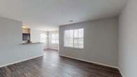 This single-floor residence offers a clean, contemporary design with a neutral color palette and thoughtful layout throughout. The open-concept living and dining area is anchored by rich, dark hardwood-style flooring that extends seamlessly across the main living spaces. Large windows dressed with horizontal blinds fill the area with natural light, while a decorative chandelier above the dining space adds a refined touch. A breakfast bar connects the dining area to the kitchen, which features dark espresso cabinetry, granite-style countertops, and black appliances including a refrigerator, electric range, and built-in microwave. The kitchen's hardwood-style flooring continues the cohesive aesthetic of the main living area. The bedrooms offer plush carpeting, neutral walls, and windows that provide ample natural light. Each room offers generous proportions suitable for a variety of furnishing arrangements. The bathrooms are well-finished: one features a glass-enclosed shower stall with tile surround and dark wood vanity cabinetry, while the second includes a full tub-shower combination with tile surround, tile flooring, and a white vanity countertop. Overall, the space presents a move-in-ready environment with consistent, practical finishes throughout.