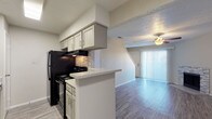 This two-story unit at 1501 E Mockingbird Lane in Victoria, Texas is thoughtfully designed across two distinct levels. The main floor centers on an open-concept layout where the kitchen flows directly into the living and dining areas. The kitchen is well-appointed with gray cabinetry, stone tile backsplash, light granite-style countertops, black appliances, and a peninsula that separates the cooking space from the adjoining dining area. Wood-style flooring extends throughout the main level, complementing the neutral color palette. The living room is a standout space, featuring a stone-surround fireplace, a ceiling fan with integrated lighting, and a sliding glass door that allows natural light to fill the room. A staircase leads to the upper level, where carpeted bedrooms offer a quieter, more comfortable atmosphere. The upper floor also includes windows that bring in natural light and a full bathroom outfitted with gray cabinetry, stone-look tile surround, and wood-style flooring. Textured ceilings are consistent throughout, and the overall design maintains a clean, contemporary aesthetic with practical finishes across both floors.