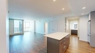 Located along the Long Beach waterfront, this modern 2-bedroom, 2-bathroom residence offers a thoughtfully designed open-concept layout with high-end finishes throughout. The combined kitchen and living area serves as the heart of the home, anchored by a striking central island with a bold teal base and white quartz countertop. The kitchen is fully equipped with stainless steel appliances, light blue flat-front cabinetry, a subway tile backsplash, and warm wood-look flooring that extends into the living area. Both bedrooms feature plush carpeting and expansive floor-to-ceiling windows that frame breathtaking views of the Pacific Ocean, Long Beach Marina, and the surrounding beachfront. Natural light pours generously into every room, creating a bright, airy ambiance throughout. The primary bathroom is a refined retreat with a glass-enclosed walk-in shower, mosaic tile flooring, warm wood-tone cabinetry, dual sinks, and a backlit vanity mirror. The second bathroom mirrors the same contemporary aesthetic with sleek gray cabinetry and a backlit mirror. A dedicated closet provides practical storage, completing this well-appointed coastal residence.