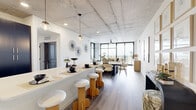 This well-appointed single-floor residence offers a thoughtfully designed layout encompassing three bedrooms, three bathrooms, a dedicated office, and a combined kitchen and living area. The interior is defined by a striking exposed concrete ceiling that runs throughout the main living spaces, lending an industrial-modern character that contrasts elegantly with crisp white walls and light wood-tone flooring found throughout.

The open-concept kitchen and living area serves as the heart of the home. The kitchen features dark, flat-panel cabinetry paired with white quartz countertops, stainless steel appliances, and a spacious island with bar seating. Pendant lighting and a white subway tile backsplash add refined detail. The living and dining areas extend naturally toward floor-to-ceiling windows, flooding the space with natural light and offering expansive outdoor views.

The bedrooms are generously proportioned, with the primary suite benefiting from large black-framed windows that frame scenic elevated views. The three bathrooms are finished with clean, modern fixtures, walk-in glass showers, hexagonal tile flooring, and dark vanities with white countertops. The dedicated office includes built-in shelving, providing a functional and organized workspace. Two closets, including a walk-in with wire shelving systems, offer practical storage. A stylishly appointed hallway with a floating wood shelf and large mirror completes the space.