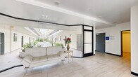Located on Laurel Canyon Boulevard in the Valley Village neighborhood of Los Angeles, this building's lobby and hallway spaces offer a clean, contemporary first impression. The entry corridor is finished with large-format light stone-look tile flooring that runs throughout, complementing the crisp white walls and dark-framed glass partitions that define the space's modern aesthetic.

The main lobby features floor-to-ceiling glass walls that frame views of an open interior courtyard, filling the space with abundant natural light. A seating area with a white leather sofa and a decorative side table with fresh flowers adds a welcoming touch. The glass-enclosed design creates a seamless visual connection between the interior and the landscaped courtyard beyond.

The secondary hallway serves as a functional entry point from Laurel Canyon Boulevard, with glass doors, a built-in mailbox station, and direct access to the building's interior corridors. Exterior elements include striking green marble cladding at the building facade, lush landscaping, and glass-railed balconies visible above, contributing to the building's polished curb appeal.

Together, the lobby and hallways establish a well-maintained, modern environment with thoughtful design details, ample natural light, and a seamless flow between the exterior streetscape and the building's interior common areas.