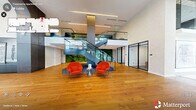 Located at 500 E Main St in downtown Durham, NC, this impressive lobby offers a generously scaled, single-floor layout that makes an immediate architectural statement. The double-height ceilings flood the space with natural light through floor-to-ceiling steel-framed windows, creating an open and airy atmosphere throughout.

The centerpiece of the lobby is a sculptural floating staircase with glass railings, flanked by a lush living green wall that adds a striking biophilic element. Warm-toned hardwood flooring runs across the main areas, contrasting elegantly with polished concrete and geometric tile accents in adjacent zones. A staffed reception desk anchors one end of the lobby, surrounded by curated seating arrangements featuring designer chairs and tasteful greenery.

The space includes multiple glass-enclosed private offices and meeting rooms framed in bold black steel, offering transparency while maintaining functionality. A large conference table serves as a collaborative hub, while sculptural art pieces and framed works adorn the walls throughout. An elevator bank with dark paneling and a warm wood-paneled ceiling provides vertical access to upper floors. The overall ambiance is sophisticated and modern, blending contemporary design with refined materials to create a welcoming and professional environment.