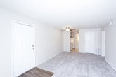 This single-floor unit offers a straightforward, functional layout with a neutral color palette of warm beige tones throughout. The spacious main living area features plush wall-to-wall carpeting, a ceiling fan with light fixture, and a sliding glass door dressed with vertical blinds that allows abundant natural light to fill the room. A front entry door with hardwood-style flooring at the threshold transitions seamlessly into the carpeted living space, which also connects directly to the kitchen.

The kitchen is compact yet practical, equipped with a Whirlpool electric coil range, an overhead ventilation hood, a refrigerator, and ample white cabinetry providing generous storage. Light countertops complement the cabinetry for a clean, cohesive look.

The bedrooms are carpeted and finished in the same warm neutral tones. One bedroom features a single window with blinds, while another benefits from dual windows that invite natural light from multiple angles, creating a bright and airy atmosphere.

The bathroom includes a full tub and shower combination with white square wall tiling, a chrome curtain rod, a toilet, and a vanity with countertop. Ceramic tile flooring completes the space with a practical, easy-to-maintain finish. Overall, the unit presents a clean, move-in ready environment.