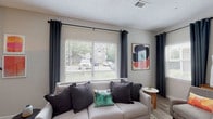 Located at 100 Northwoods Dr in Cary, NC, this single-floor residence offers a thoughtfully designed layout across several distinct living areas. The living room serves as a welcoming focal point, featuring wood-style plank flooring, a textured ceiling, and large windows dressed with floor-to-ceiling dark curtains that frame views of the surrounding neighborhood while drawing in generous natural light. A ceiling fan and fireplace add comfort and character to the space.

The kitchen is well-equipped with white cabinetry, granite-style countertops, a grey subway tile backsplash, and black appliances including a range, microwave, and dishwasher. A window above the sink provides additional natural light. The unit also includes an in-unit laundry area, adding everyday convenience.

The bedrooms are carpeted and comfortably scaled, each featuring windows with blinds and curtains, ceiling fans, and closet access. The bathrooms are finished with wood-style flooring, white fixtures, and granite-topped vanities with undermount sinks, complemented by a tub-shower combination. The overall aesthetic throughout is clean, neutral, and modern.