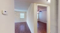 Located at 110 Kendra Way in Palm Harbor, Florida, this single-story home offers a practical and comfortable layout with consistent wood-look flooring throughout. The living area is generously sized, featuring a ceiling fan with light kit, multiple windows with horizontal blinds, and a sliding glass door that floods the space with natural light. The open feel of the main living space transitions smoothly into the adjacent rooms, each finished with the same warm-toned flooring, ceiling fans, and window treatments that provide a cohesive look throughout the home. The kitchen is well-appointed with light wood cabinetry, dark granite-style countertops, a decorative tile backsplash, and a full suite of black appliances including a refrigerator, electric range, microwave, and dishwasher. A closet with louvered doors offers convenient pantry or storage space just off the kitchen. The bathroom features a vanity with light wood cabinetry, a dark countertop, a framed mirror, and bright overhead lighting. Textured ceilings are present throughout the home. The overall ambiance is clean, neutral, and move-in ready, making this Palm Harbor residence a functional and inviting space.