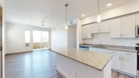This single-floor residence offers a thoughtfully designed layout across three bedrooms, one full bathroom, and a combined living and kitchen area connected by two hallways. The open-concept kitchen serves as a central feature, equipped with stainless steel appliances including a refrigerator, range, and microwave, complemented by white shaker cabinetry extending to the ceiling and granite countertops. A large kitchen island with pendant lighting provides additional workspace and casual dining potential, while the adjoining living area opens to a private balcony through sliding glass doors and benefits from a ceiling fan overhead.

Wood-look plank flooring runs consistently throughout the residence, lending a cohesive and modern aesthetic. Each bedroom features natural light through large, blinds-fitted windows, with ceiling fans adding comfort. One bedroom offers direct balcony access via a sliding door, while another includes a sliding-door closet for built-in storage.

The bathroom is finished with a dual-sink vanity topped with granite, white cabinetry, a walk-in shower with built-in shelving, and wood-look flooring. A dedicated laundry area with in-unit washer and dryer connections is also present, adding everyday convenience to this well-finished residence.