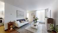 This thoughtfully laid-out single-floor unit comprises four distinct areas: a living room, kitchen, bedroom, and entrance. The living room serves as the centerpiece of the space, bathed in natural light streaming through large floor-to-ceiling sliding glass doors that open to an outdoor area. White walls and smooth ceilings amplify the brightness, while wood-tone flooring near the entrance transitions to soft carpeting in the lounge area, adding warmth and texture. The kitchen is efficiently designed with grey cabinetry, white countertops, and stainless steel appliances — including a full-size refrigerator and electric range — set atop wood-look flooring, offering a clean and functional cooking space. The bedroom is a comfortably sized, carpeted retreat with crisp white walls, a closet, and room for a full bedroom suite. It features soft natural light that creates a calm, restful atmosphere. The entrance provides a welcoming transition into the main living areas. Throughout the unit, a consistent neutral color palette of whites and warm beiges creates a cohesive, airy ambiance that maximizes the sense of space across the entire floor plan.