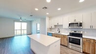Located at 3600 W Happy Valley Rd in Phoenix, AZ, this thoughtfully designed two-bedroom, two-bathroom residence offers a clean, contemporary aesthetic throughout its well-appointed single-floor layout. The open-concept kitchen and living area serves as the heart of the home, featuring a central island with a white quartz countertop, two-tone cabinetry with white uppers and warm wood-grain lowers, a subway tile backsplash, and a full suite of stainless steel appliances including a refrigerator, range, microwave, and dishwasher. Wood-look plank flooring flows seamlessly throughout the entire unit, adding warmth and visual continuity. The living area is illuminated by recessed lighting and a ceiling fan, and opens directly to a private patio through sliding glass doors, offering views of the surrounding mountain landscape. Both bedrooms are well-sized and bright, with large windows that capture natural light and scenic outdoor views. The primary bedroom includes a spacious walk-in closet with built-in shelving and hanging rods. The primary bathroom features a dual-sink vanity with wood-grain cabinetry, white countertops, and a tiled shower-tub combination. Additional highlights include four closets for ample storage, an in-unit laundry area, and a dedicated patio — rounding out a functional, modern living experience.