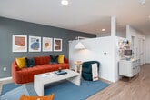 This well-appointed single-floor residence showcases a thoughtful modern design with clean lines and a cohesive aesthetic throughout. The galley-style kitchen is a standout feature, outfitted with dark charcoal cabinetry, warm brass hardware, white quartz countertops, a classic subway tile backsplash, and a full suite of stainless steel appliances including an electric range, built-in microwave, dishwasher, and refrigerator. Under-cabinet lighting adds a polished, functional touch to the workspace.

The open layout leads into a bright and inviting living area, where oversized windows frame expansive outdoor views of surrounding treetops and the broader neighborhood skyline. Light wood-style flooring flows consistently throughout the unit, enhancing the sense of openness and continuity.

The living space is generously proportioned, with a teal accent wall and abundant natural light creating a vibrant, welcoming ambiance. A bedroom area is also present, tucked alongside the main living zones within the single-floor plan.

The bathroom is finished in a clean, minimalist style with light wood-toned flooring, a dark vanity with white countertop, a soaking tub with shower combination, and neutral white walls that maintain the unit's crisp, contemporary character.