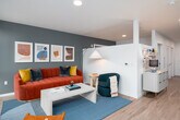 This well-appointed single-floor residence showcases a thoughtful modern design with clean lines and a cohesive aesthetic throughout. The galley-style kitchen is a standout feature, outfitted with dark charcoal cabinetry, warm brass hardware, white quartz countertops, a classic subway tile backsplash, and a full suite of stainless steel appliances including an electric range, built-in microwave, dishwasher, and refrigerator. Under-cabinet lighting adds a polished, functional touch to the workspace.

The open layout leads into a bright and inviting living area, where oversized windows frame expansive outdoor views of surrounding treetops and the broader neighborhood skyline. Light wood-style flooring flows consistently throughout the unit, enhancing the sense of openness and continuity.

The living space is generously proportioned, with a teal accent wall and abundant natural light creating a vibrant, welcoming ambiance. A bedroom area is also present, tucked alongside the main living zones within the single-floor plan.

The bathroom is finished in a clean, minimalist style with light wood-toned flooring, a dark vanity with white countertop, a soaking tub with shower combination, and neutral white walls that maintain the unit's crisp, contemporary character.