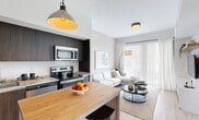 Located at 22555 SW 107th Ave in Miami, FL, this well-appointed single-floor unit offers a modern, efficiently designed layout that maximizes every square foot. The open-plan kitchen and living area serves as the heart of the home, anchored by a sleek kitchen outfitted with dark wood cabinetry that extends floor to ceiling, granite countertops, stainless steel appliances including a French door refrigerator, electric range, and built-in microwave. A freestanding island with a warm butcher-block top and bar seating adds both workspace and casual dining functionality. The living area flows seamlessly from the kitchen, featuring light wood-style flooring, a wall-mounted media console with floating wood shelving, and large sliding glass doors dressed with vertical blinds that invite generous natural light. The bedroom is a calm, neutral retreat with textured accent wallpaper, natural light from a window with sheer curtains, built-in wood shelving, and a dedicated media area. A full bathroom features a granite-topped vanity with dark wood cabinetry, a tub-shower combo, and light wood flooring. A spacious closet with floor-to-ceiling white cabinetry, an in-unit laundry area, and a utility room round out the practical offerings of this contemporary Miami residence.