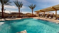 This expansive outdoor space in Phoenix, Arizona, features a stunning resort-style pool as its centerpiece. The large, irregularly shaped pool boasts crystal-clear turquoise water, inviting residents to cool off from the desert heat. Surrounding the pool area are numerous amenities designed for relaxation and socialization. Multiple palm trees dot the landscape, providing a tropical ambiance and natural shade. Comfortable lounge chairs line the pool's edge, perfect for sunbathing or reading. A covered cabana area offers shaded seating for those seeking respite from the sun. The space also includes additional seating areas with tables and chairs, ideal for outdoor dining or gatherings. The architecture of the surrounding buildings features a Mediterranean-inspired style with tile roofs and neutral-toned stucco walls. This thoughtfully designed outdoor space creates a luxurious, vacation-like atmosphere for residents to enjoy year-round, seamlessly blending relaxation and community in the heart of the Arizona desert.
